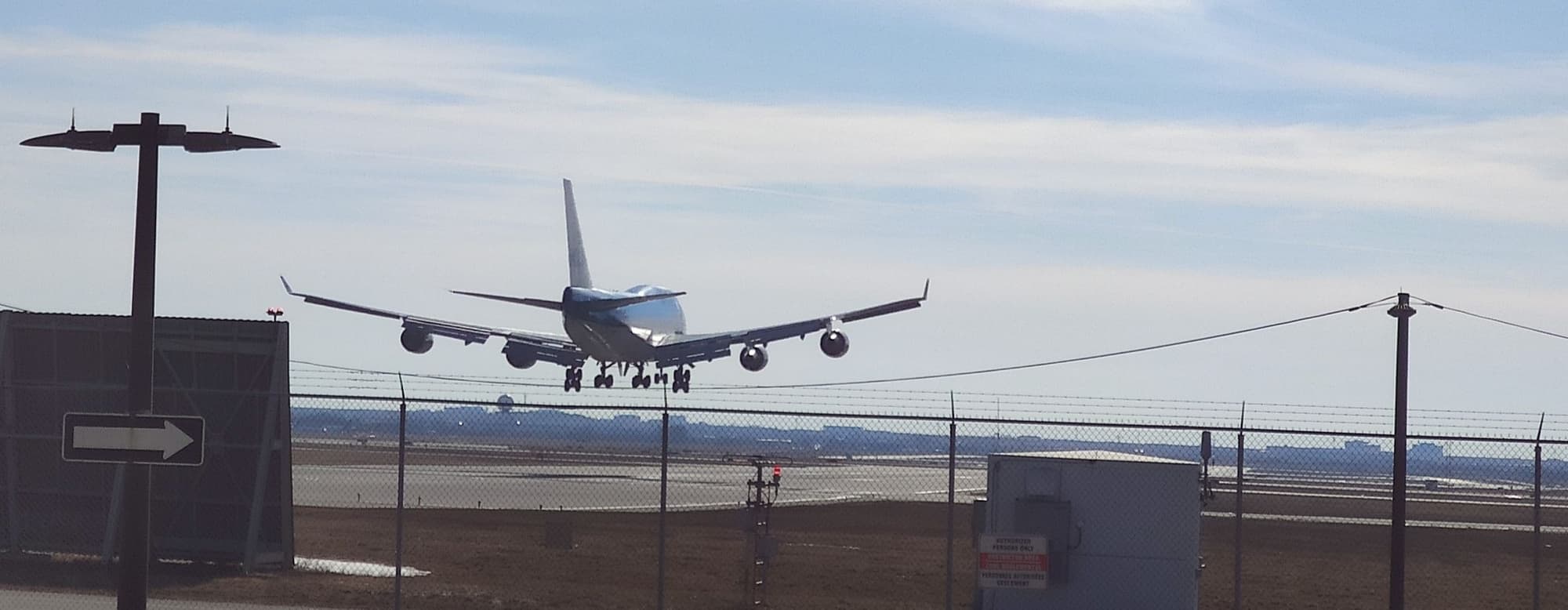The KLM 747-400 seconds from touchdown, seen head-on through the perimeter fence across the runway.